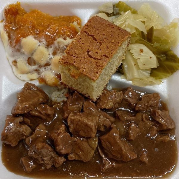 Southern meal with beef tips and gravy, rice, cornbread, collard greens, and sweet potato casserole.
