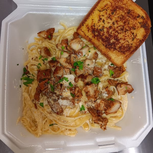 Southern-style pasta with fried chicken, creamy sauce, and a slice of garlic toast in a to-go container.