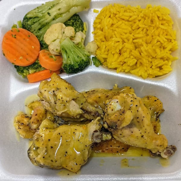 Southern-style chicken wings with yellow rice, broccoli, cauliflower, and carrots in a takeout container.