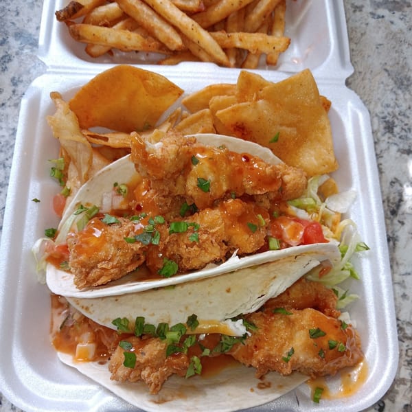 Southern-style fried chicken tacos with sauce, lettuce, and tomatoes, served with fries and chips.