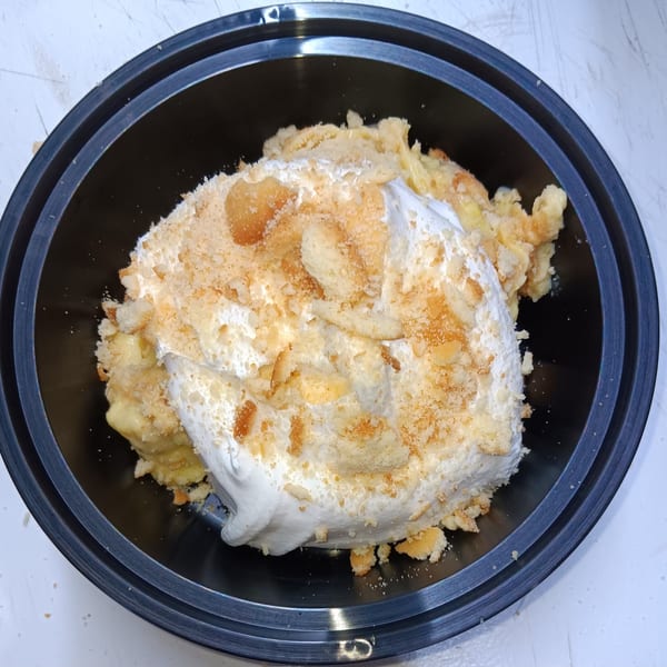 Southern banana pudding with whipped cream and vanilla wafer crumbles in a black bowl.