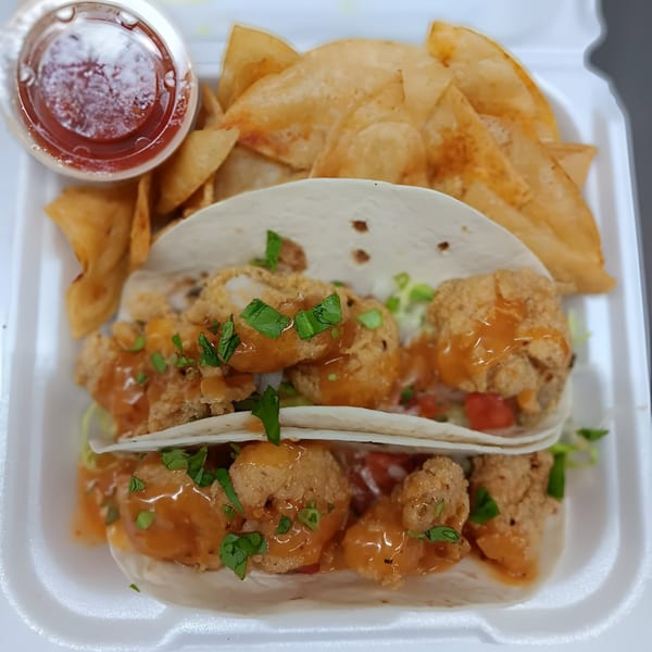 Two southern-style shrimp tacos with sauce and cilantro, served with tortilla chips and a side of salsa.